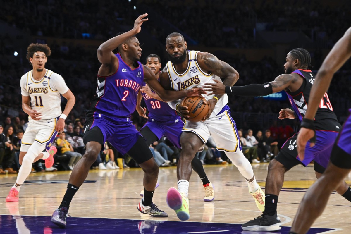 Nov 10, 2024; Los Angeles, California, USA; Los Angeles Lakers forward LeBron James (23) drives the ball against Toronto Raptors forward Jonathan Mogbo (2) and guard Jamal Shead (23) during the first half at Crypto.com Arena.