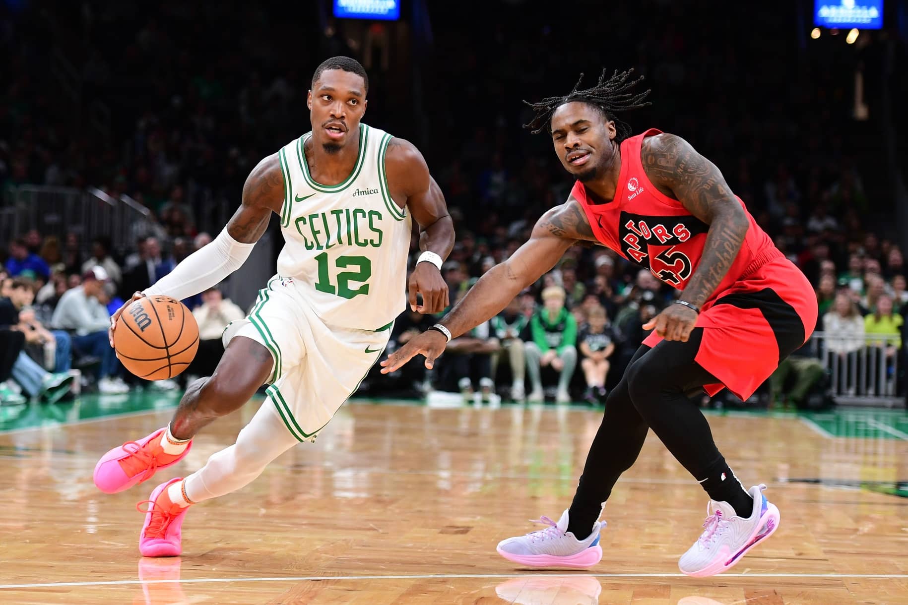 Oct 13, 2024; Boston, Massachusetts, USA; Boston Celtics guard Lonnie Walker IV (12) controls the ball while Toronto Raptors guard Davion Mitchell (45) defends during the first half at TD Garden. Mandatory Credit: Bob DeChiara-Imagn Images