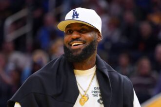 San Francisco, California, USA; Los Angeles Lakers forward LeBron James (23), wearing a Los Angeles Dodgers hat, watches from the sideline during a break against the Golden State Warriors in the third quarter at Chase Center. Mandatory Credit: David Gonzales-Imagn Images