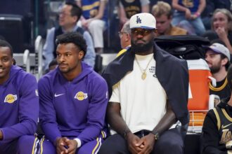 Los Angeles Lakers guard Bronny James (9) and forward LeBron James (23), wearing a Los Angeles Dodgers cap, watch the action against the Golden State Warriors in the first quarter at Chase Center.