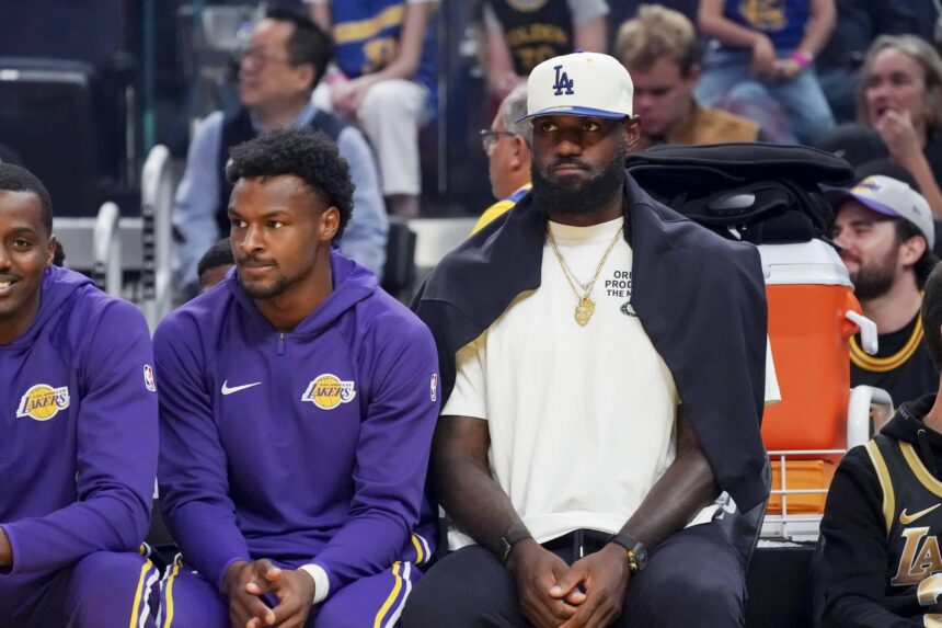 Los Angeles Lakers guard Bronny James (9) and forward LeBron James (23), wearing a Los Angeles Dodgers cap, watch the action against the Golden State Warriors in the first quarter at Chase Center.