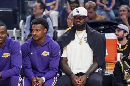 Oct 5, 2025; San Francisco, California, USA; Los Angeles Lakers guard Bronny James (9) and forward LeBron James (23), wearing a Los Angeles Dodgers cap, watch the action against the Golden State Warriors in the first quarter at Chase Center. Mandatory Credit: David Gonzales-Imagn Images