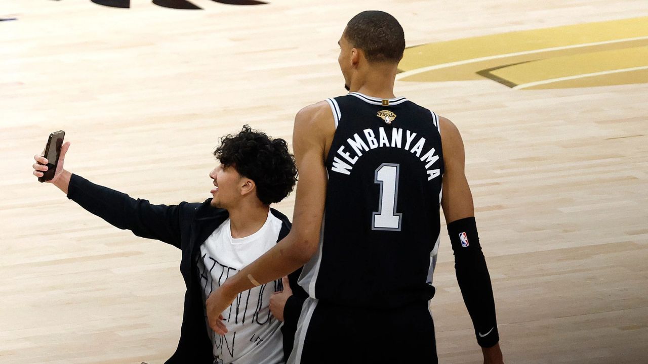 SAN ANTONIO, TEXAS - JUNE 03: A fan runs onto the court and takes a photo with Victor Wembanyama #1 of the San Antonio Spurs during the fourth quarter in Game One of the 2026 NBA Finals against the New York Knicks at Frost Bank Center on June 03, 2026 in San Antonio, Texas. (Photo by Ronald Cortes/Getty Images)