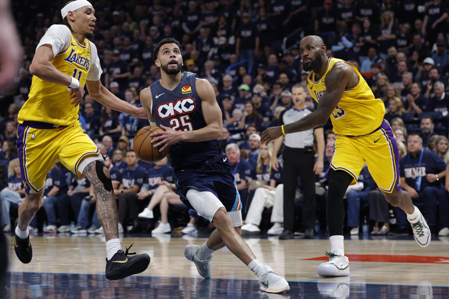 May 7, 2026; Oklahoma City, Oklahoma, USA; Oklahoma City Thunder guard Ajay Mitchell (25) drives between Los Angeles Lakers center Jaxson Hayes (11) and forward LeBron James (23) in the second half during game two of the second round of the 2026 NBA Playoffs at Paycom Center. Mandatory Credit: Alonzo Adams-Imagn Images